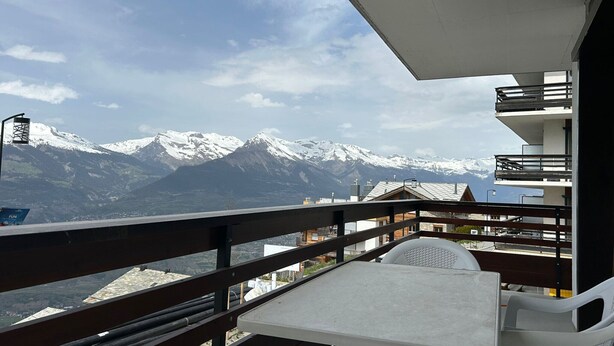 Ein Balkon mit Tisch und Stühlen mit Blick auf schneebedeckte Berge.