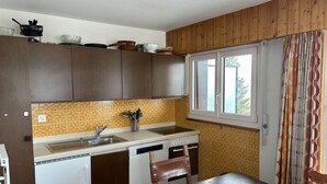 Eine kleine Küche mit Holzschränken, einer Spüle, einem Herd und einem Fenster mit Vorhängen.