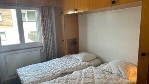 Ein Zimmer mit zwei Betten, Holzvertäfelung, einem Fenster mit Vorhängen und einer Heizung.