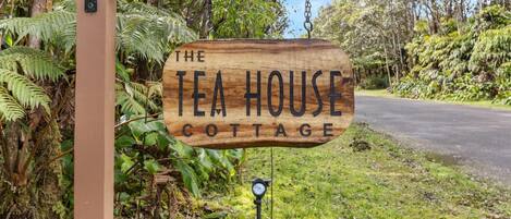 Ein hölzernes Schild mit der Aufschrift 'The Tea House Cottage' und der Nummer '11 3807' darüber.