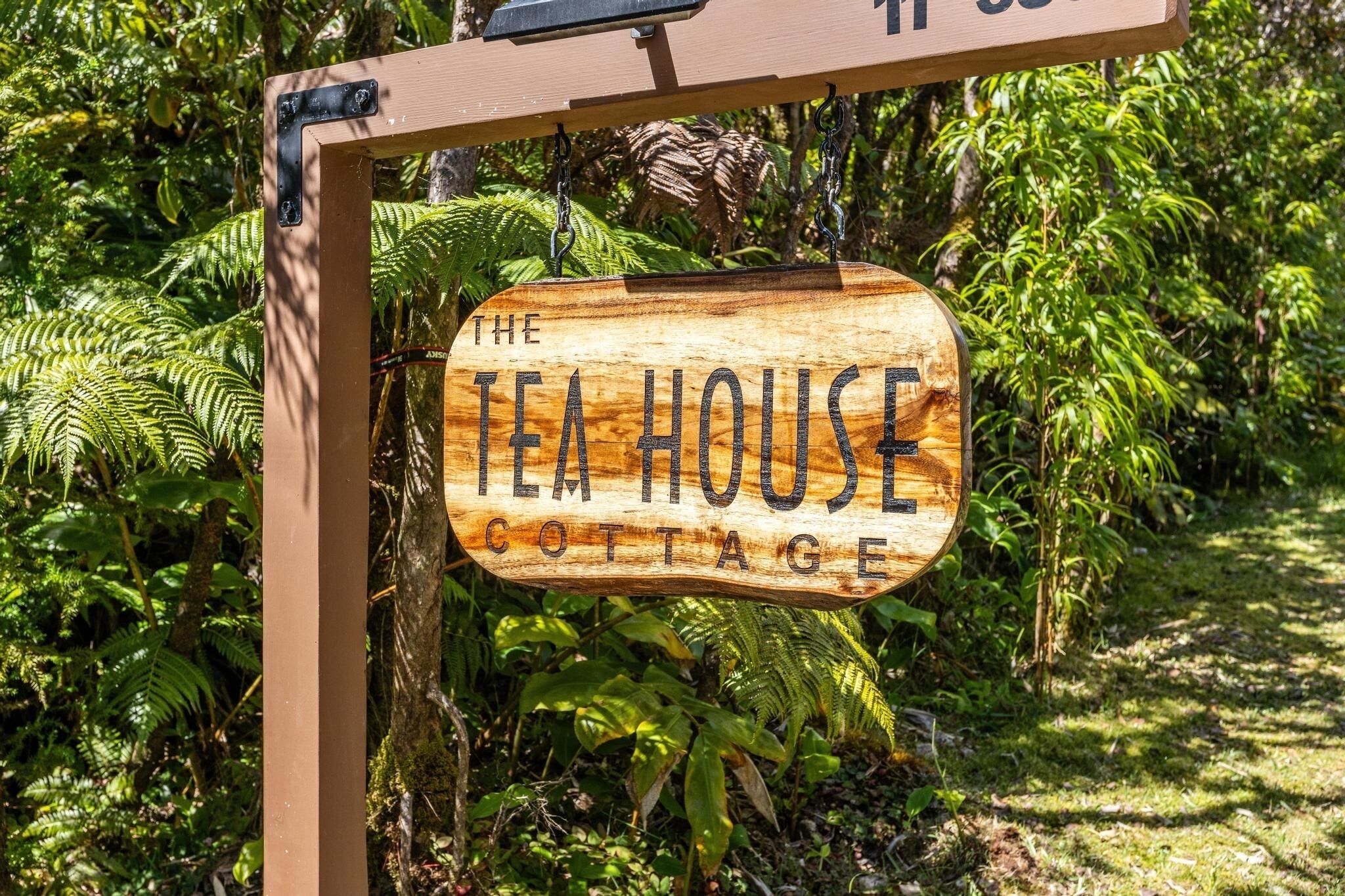 En träskylt med texten ”The Tea House Cottage” i en frodig, grön miljö.