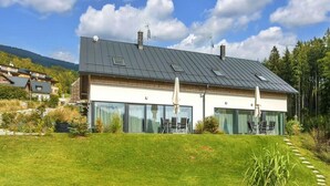 Ein modernes, zweistöckiges Haus mit geneigtem Dach, großen Schiebeglastüren und einem gepflegten Rasen.