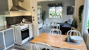 Una cocina moderna con estufa, horno y armarios blancos. Hay una mesa de comedor con sillas y una mesita auxiliar.
