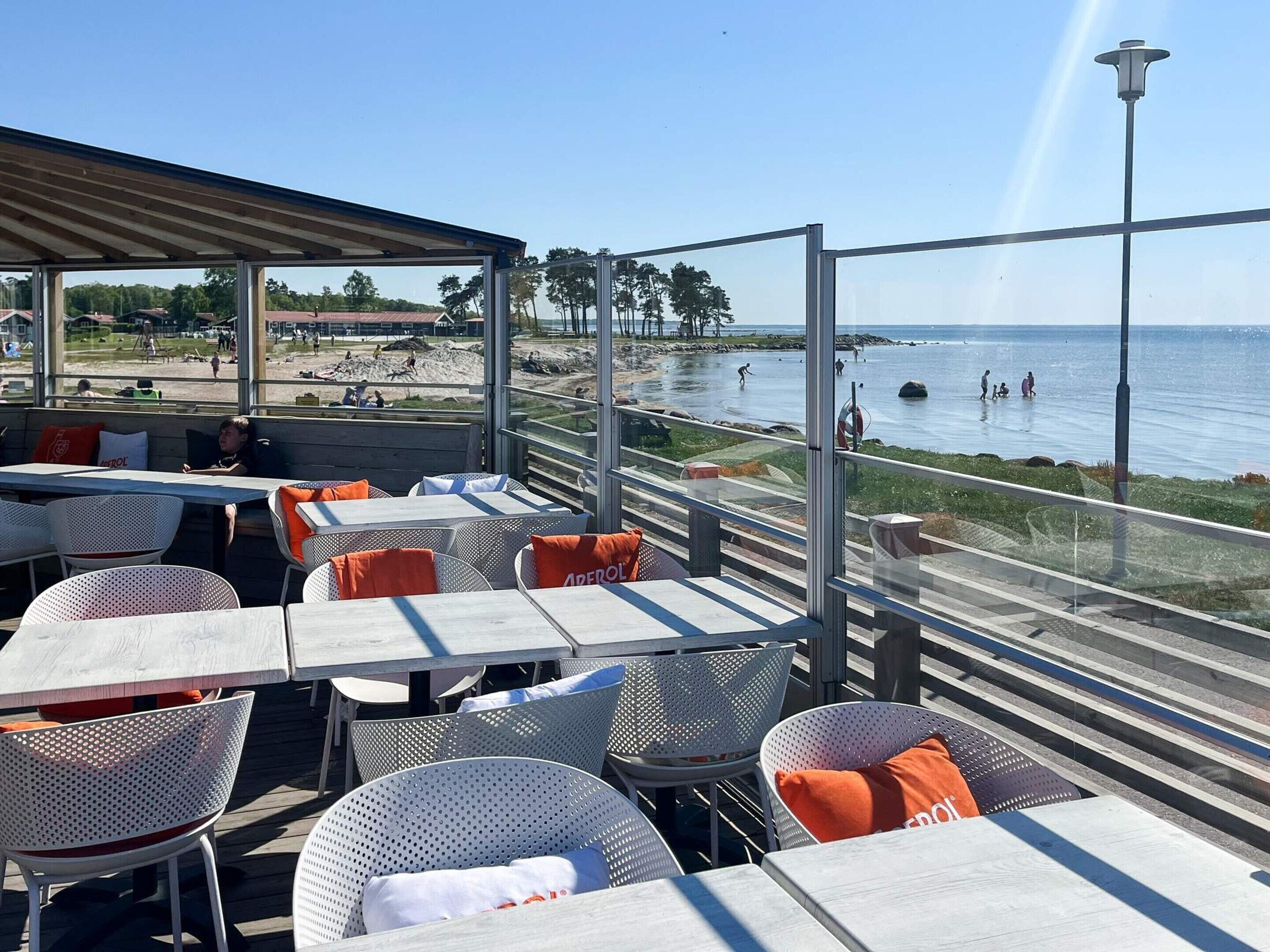 An outdoor seating area with tables and chairs, overlooking a beach and the sea.