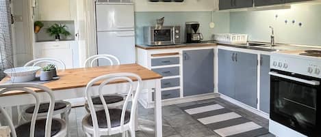 Cocina compacta con comedor, armarios blancos, microondas, estufa y un reloj en la pared.