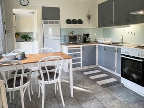 A compact kitchen with a dining area, white cabinetry, a microwave, a stove, and a clock on the wall.