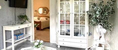 A living room with a television, a cabinet with glass doors, a white table, and a potted plant.