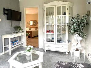 A living room with a television, a cabinet with glass doors, a white table, and a potted plant.