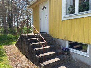 A yellow building with a white door and a window. There are concrete steps leading up to the door. - 4 Person Holiday Home in Farjestaden (Farjestaden)