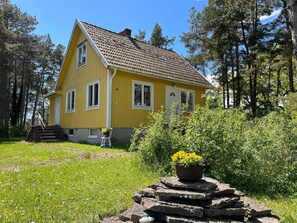 Een geel houten huis met pannendak, omringd door groen en bomen.