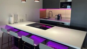 Une cuisine moderne dotée d’un îlot central, de tabourets de bar, de luminaires suspendus et d’un éclairage néon sous les meubles hauts.
