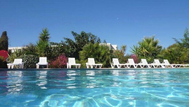 Une piscine aux eaux cristallines, bordée de chaises longues blanches, entourée d’une végétation luxuriante et de palmiers.