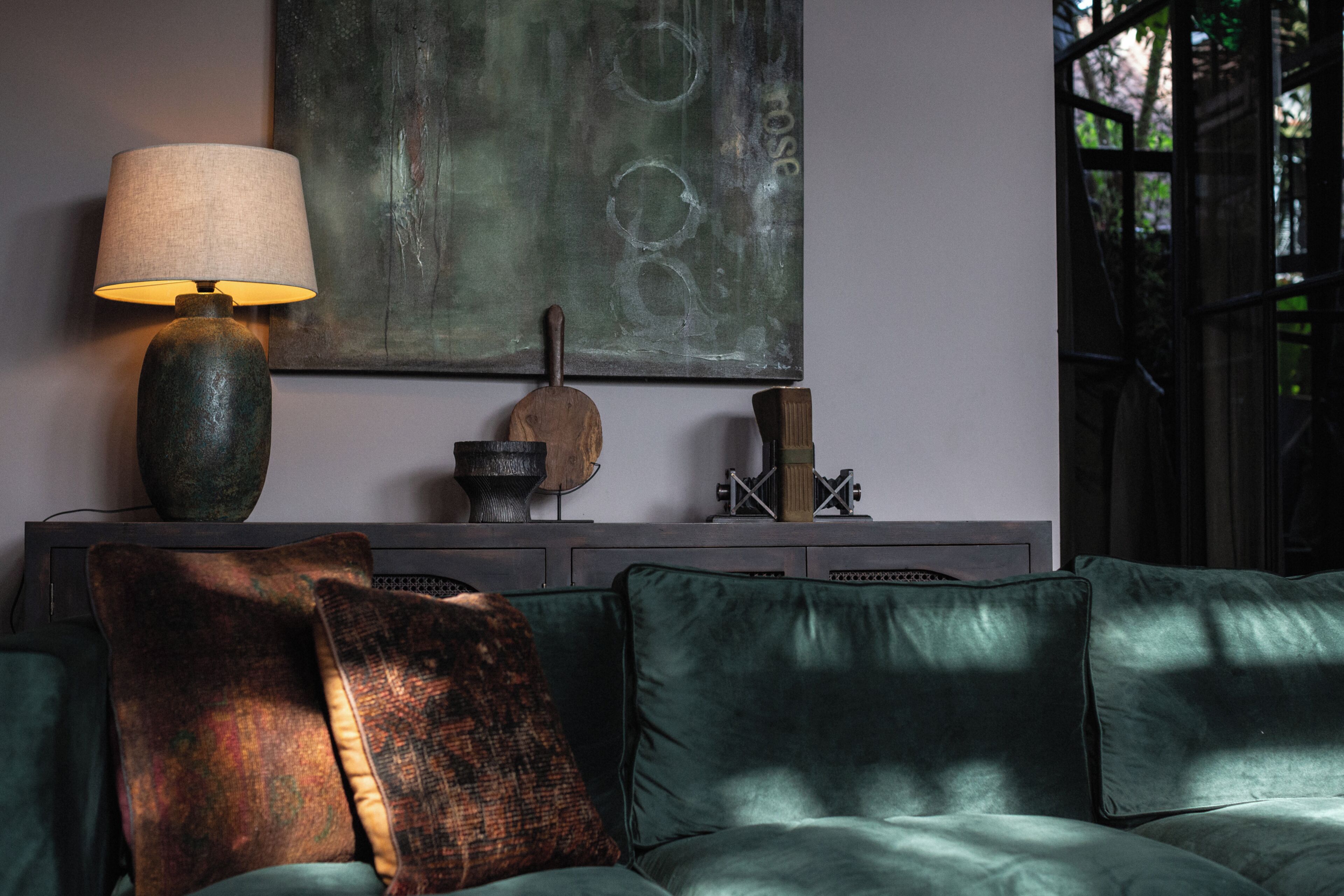 A modern living room with a green sofa, a lamp, and a painting on the wall.