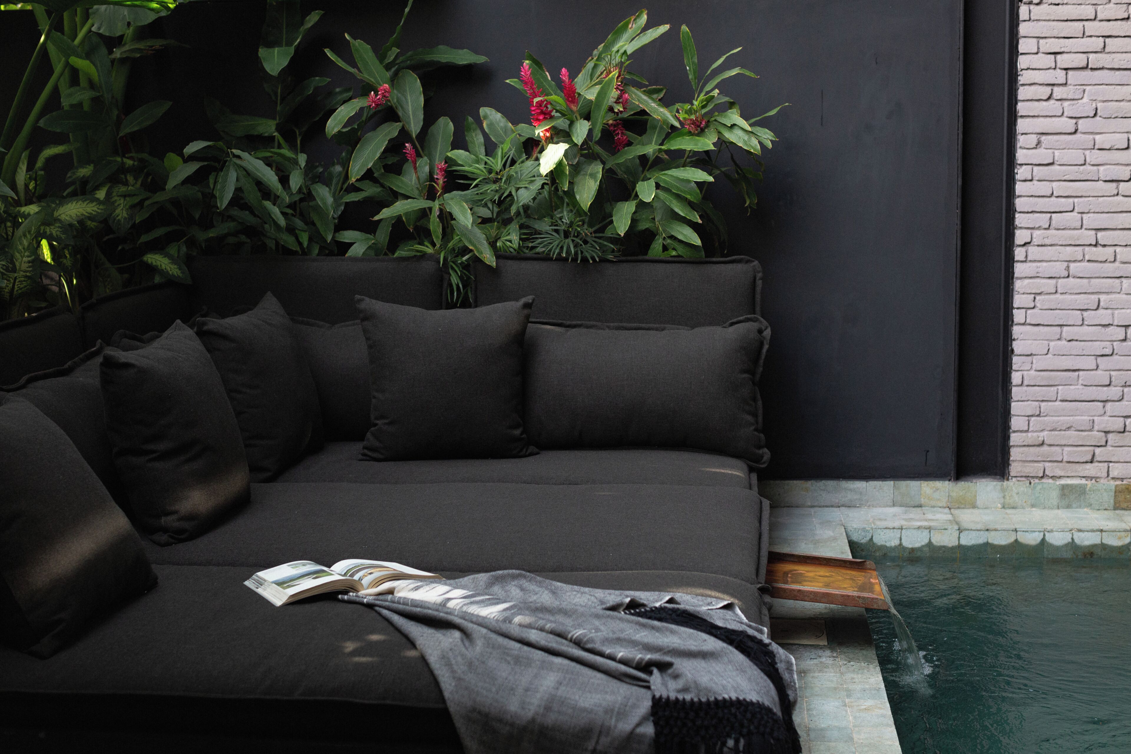Un espace extérieur moderne aménagé avec un canapé noir, un livre et une couverture.