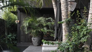 A modern outdoor area with a wooden deck, a large planter with tropical plants, a water feature, and a decorative lamp. - The Bohemian Bali, a Member of Design Hotels (Canggu)