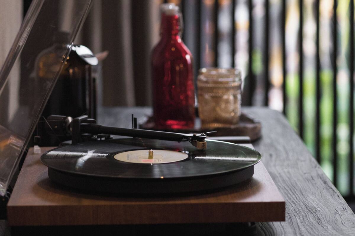 A turntable on a wooden table with a vinyl record, a red bottle, and a glass jar in the background.