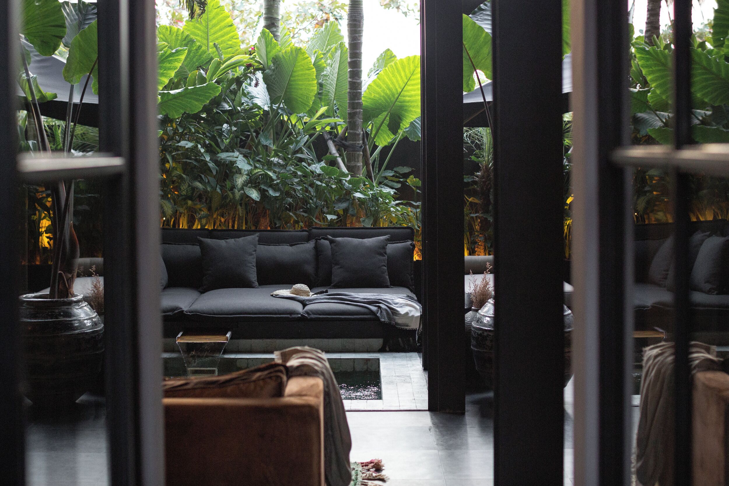 A modern living room with a sofa, coffee table, and a view of lush greenery through a glass door.