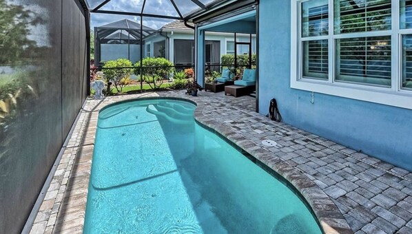 A swimming pool with a stone deck, a covered patio area, and a view of a residential building. - Luxury Lifestyle in Resort Setting (Naples)