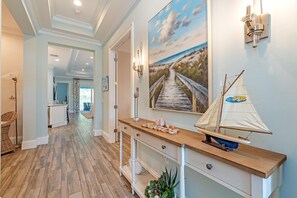 A hallway with a wooden floor, a console table with a sailboat model, and a painting of a coastal scene. - Luxury Lifestyle in Resort Setting (Naples)