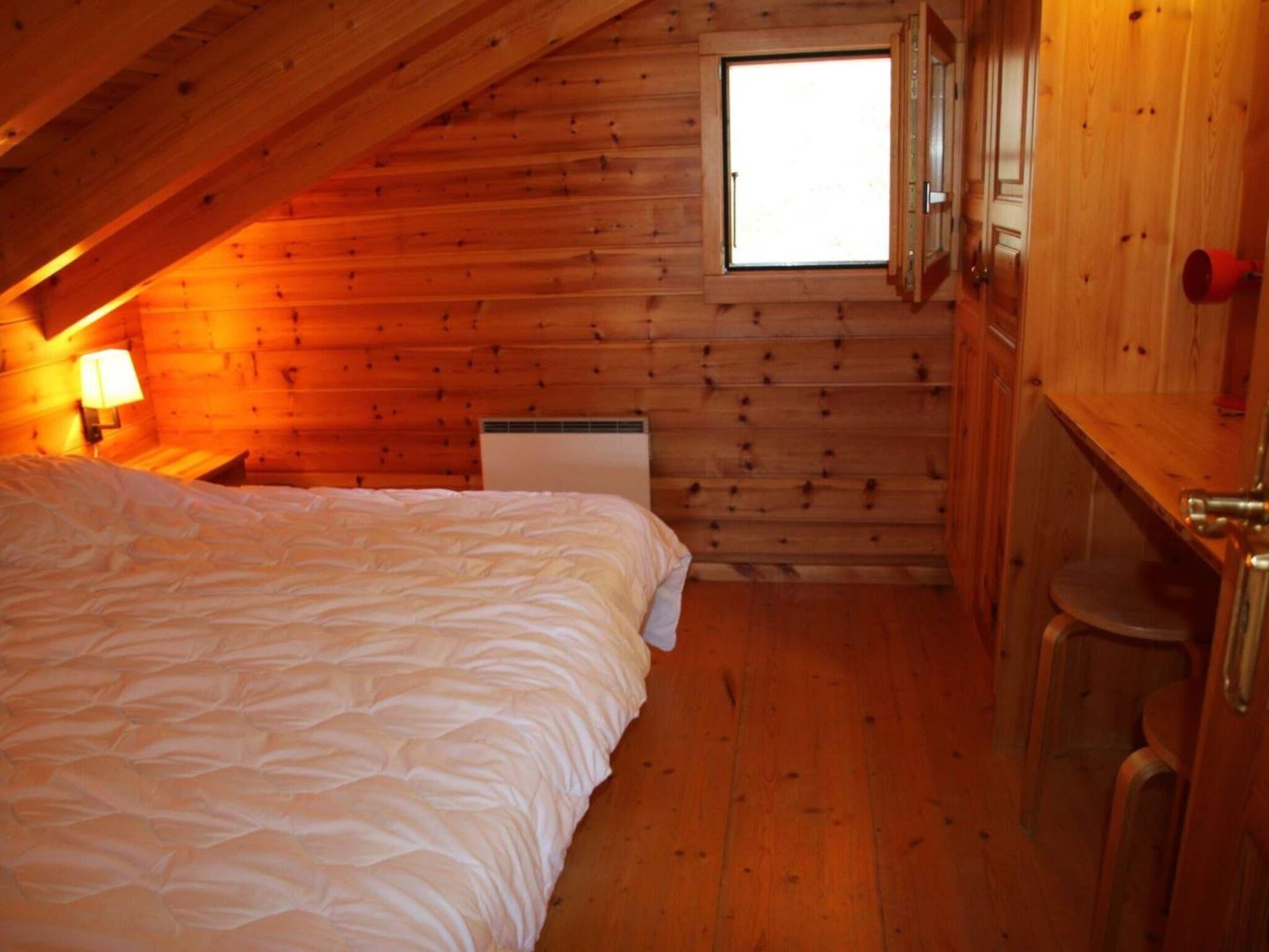 A cozy room with a bed, a window, and a wooden wall.