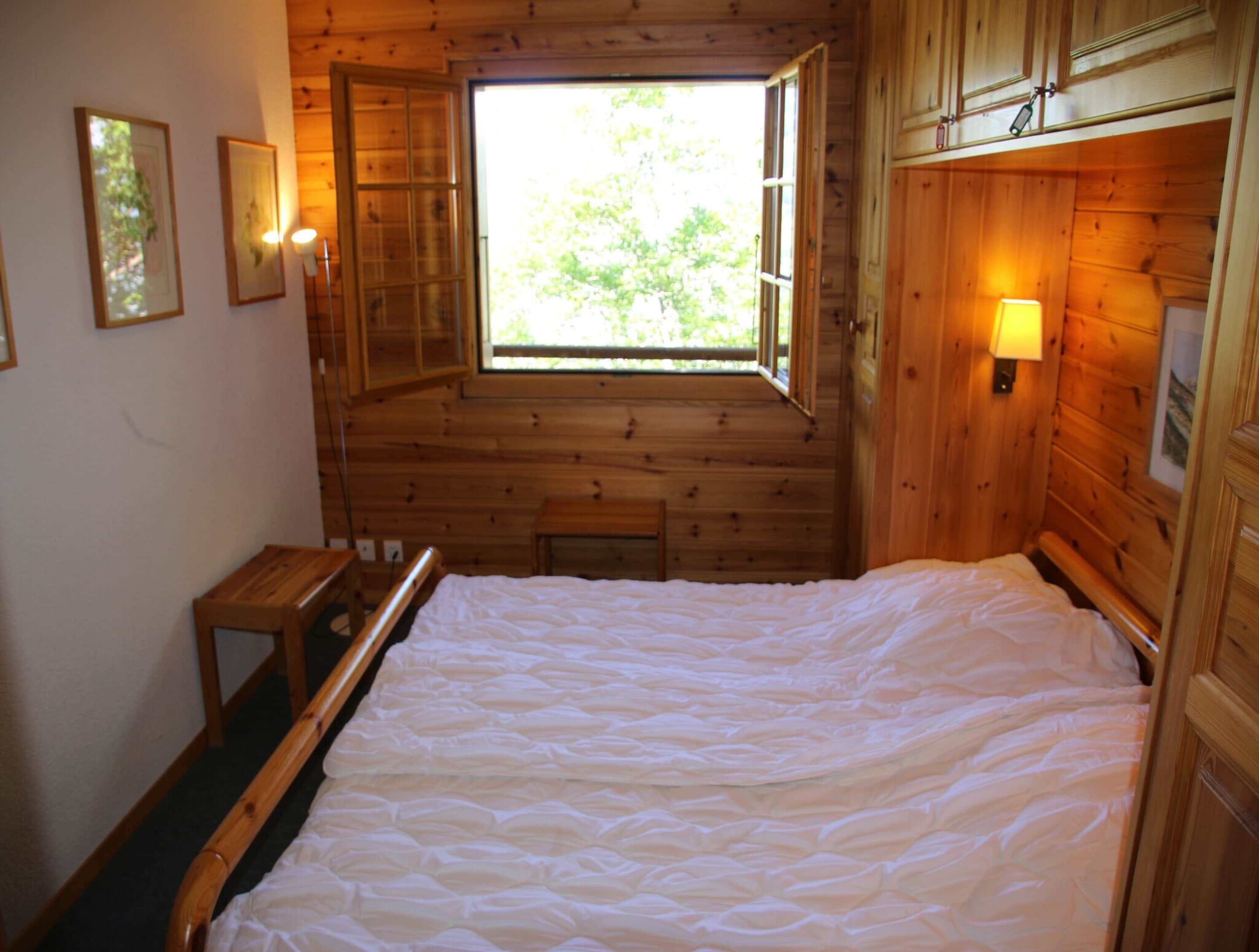 Una habitación tipo cabaña de madera con una cama grande, un ventanal y una mesita.