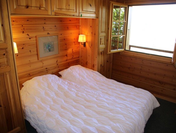 Une pièce de cabane en bois comprenant un lit, une fenêtre et une lampe fixée au mur.