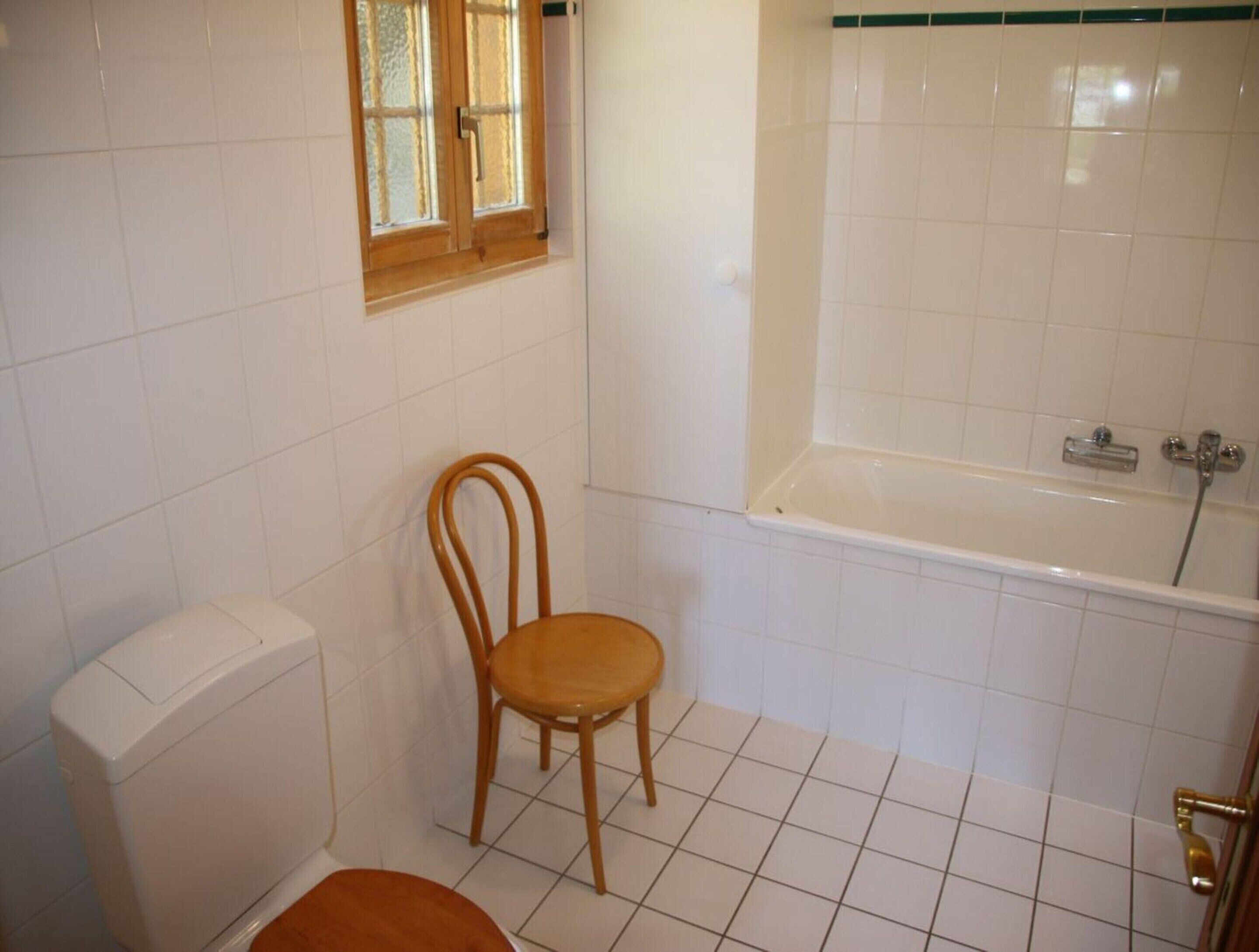 A bathroom with a toilet, a wooden chair, and a bathtub.