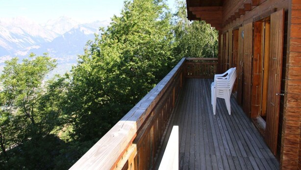 Une terrasse en bois offrant une vue sur les montagnes, un bâtiment en bois doté de plusieurs portes et une chaise blanche.