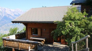 Une cabane en bois avec un toit en tuiles, une terrasse en bois et une vue sur les montagnes en arrière-plan.