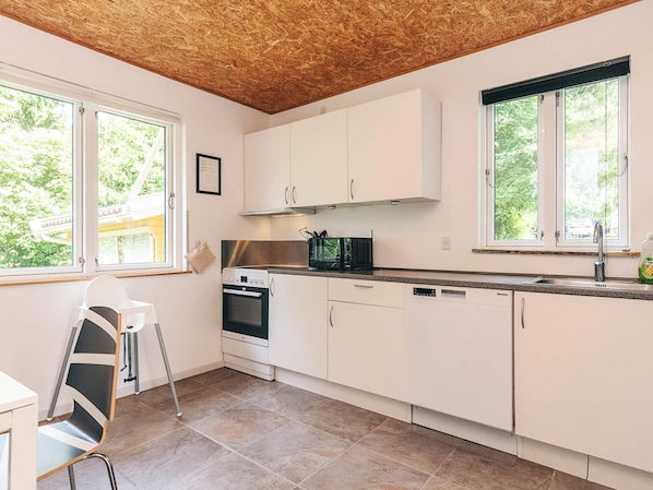 A modern kitchen with white cabinets, a stove, and a dishwasher. There are windows providing natural light and a view of greenery outside. - 6 Person Holiday Home in Borup (Borup)