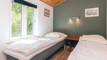 Habitación con dos camas, una ventana con vista a zonas verdes y dos luces fijadas a la pared.