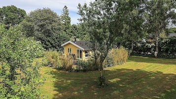 Una pequeña casa amarilla rodeada de árboles y césped.