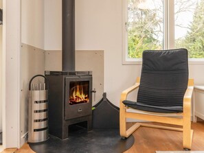 A room with a wood-burning stove, a chair, and a window with a view of trees. - 6 Person Holiday Home in Borup (Borup)