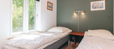 A room with two beds, a window, and a wall-mounted light fixture.