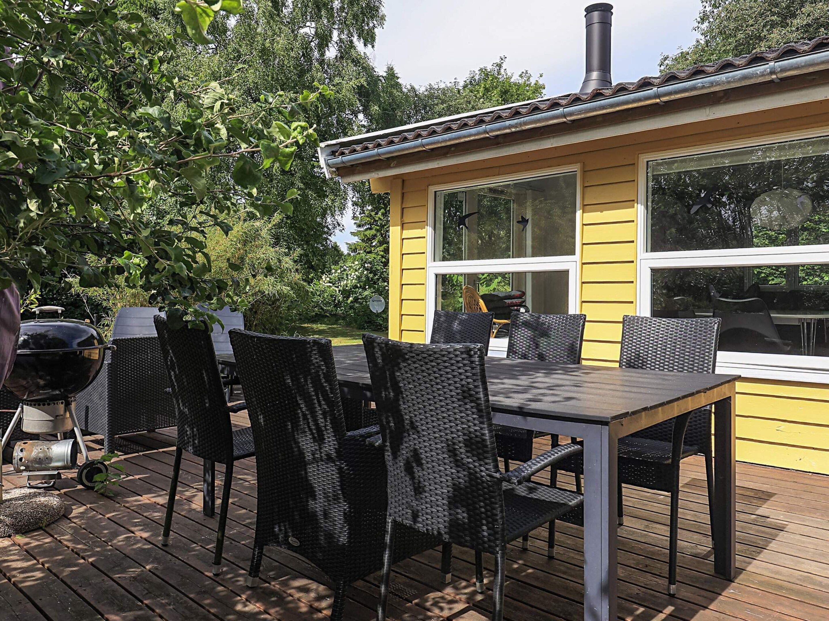 Un bâtiment jaune doté d’une terrasse, de sièges extérieurs et d’un barbecue.