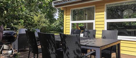 A yellow building with a deck, outdoor seating, and a barbecue grill.