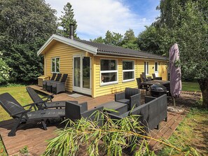 Une maison jaune avec une terrasse, du mobilier d’extérieur et un barbecue.