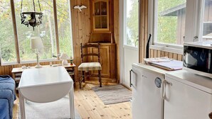 L’intérieur chaleureux d’un chalet avec une table à manger en bois, une chaise, un petit coin cuisine doté d’un réfrigérateur et une fenêtre donnant sur un paysage verdoyant.