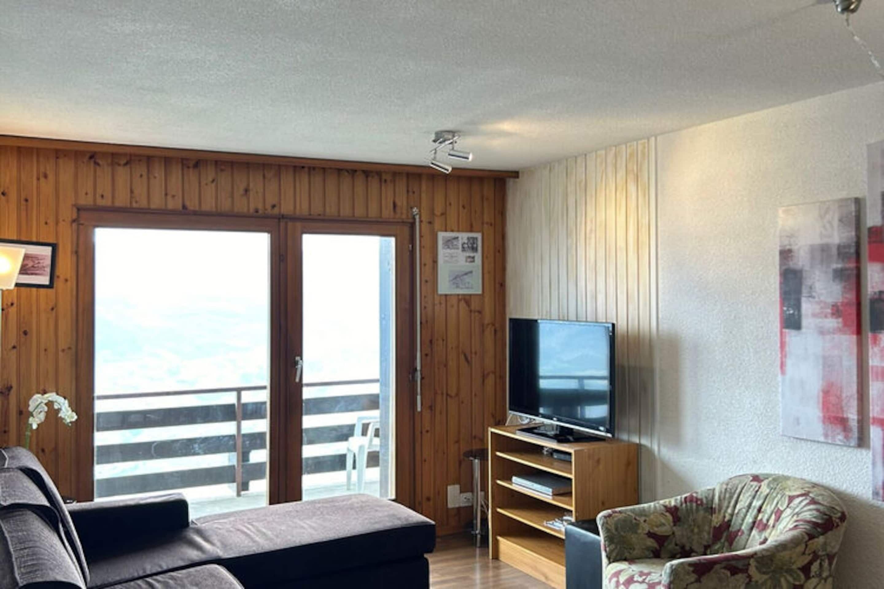 Une pièce avec un intérieur en bois, un téléviseur posé sur un meuble en bois, un canapé et un fauteuil.