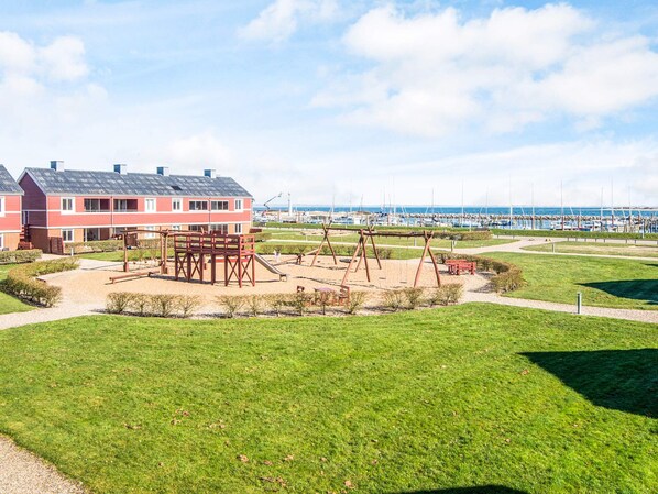 A residential area with a playground, a building with a red facade, and a marina in the background.