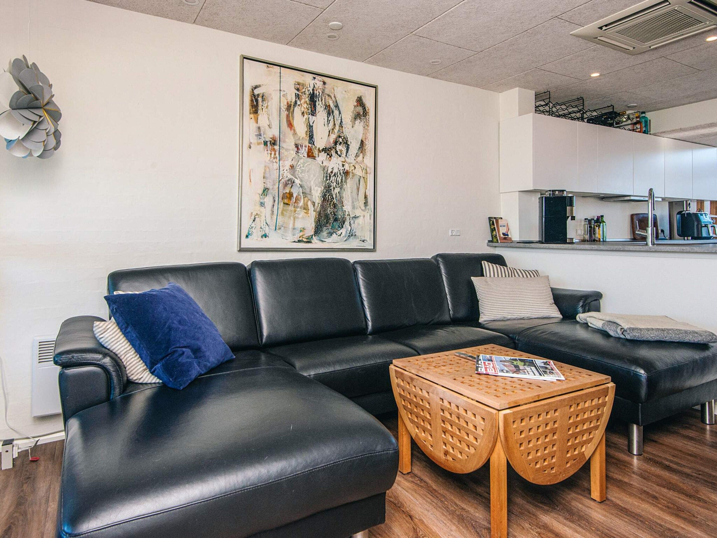 A modern living room with a black leather sofa, a wooden coffee table, and a large abstract painting on the wall.