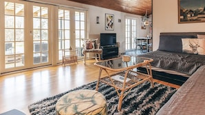 A spacious living room with a wooden ceiling, large sliding glass doors, a television, a sofa, and a dining area. - 6 Person Holiday Home in Rodby (Rodby)
