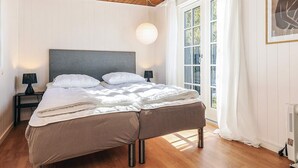 A bedroom with a wooden ceiling, a large bed with white bedding, two bedside tables with lamps, and a window with curtains. - 6 Person Holiday Home in Rodby (Rodby)