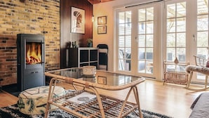 A cozy living room with a brick fireplace, a glass coffee table, and a wicker chair. - 6 Person Holiday Home in Rodby (Rodby)