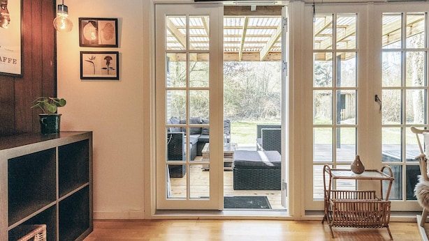 A spacious room with a wooden floor, a black console table with a plant, and a wicker chair. - 6 Person Holiday Home in Rodby (Rodby)