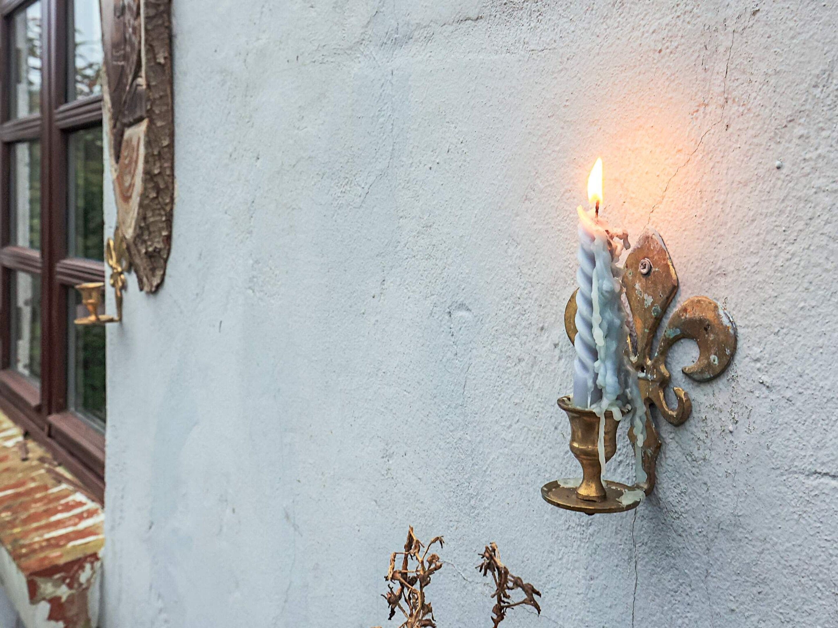 Eine Wandleuchte mit einer brennenden Kerze, ein rustikaler Fensterrahmen und eine kleine Zierpflanze.