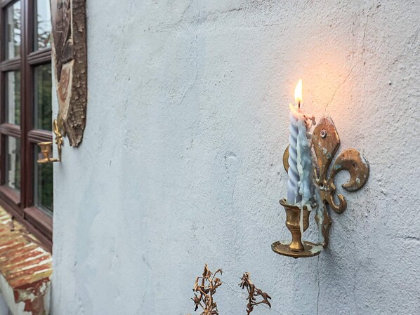 Un candelabro de pared con una vela encendida, un marco de ventana rústico y una pequeña planta decorativa.