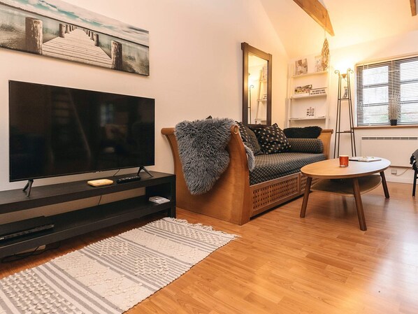 A modern living room with a large flat-screen TV, a wooden sofa, a small round table, and a decorative rug. - 5 Person Holiday Home in Saeby (Sæby)