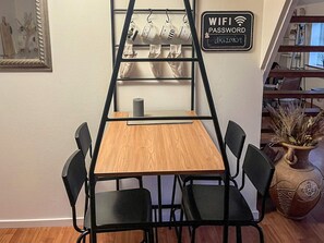 A room with a wooden table and four chairs, a black metal ladder, a wall-mounted sign with a WiFi password, and a decorative vase.