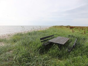 A wooden bench and table set in a grassy area with a view of the beach and dunes.